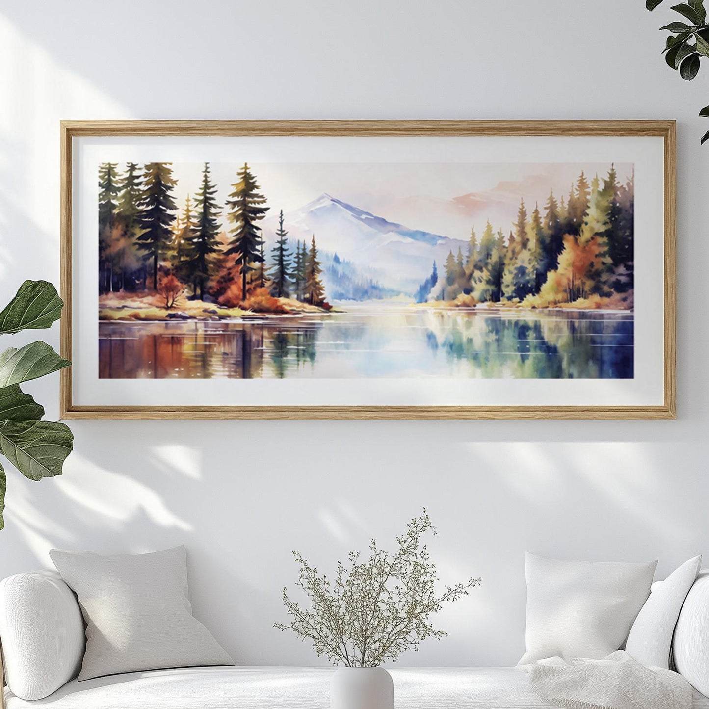 Watercolor mountain landscape artwork in a light wood frame above a white sofa