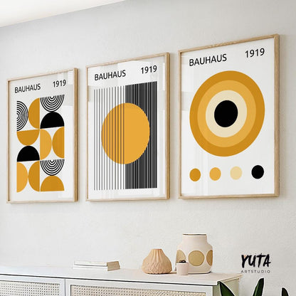 Three framed Bauhaus abstract prints in mustard yellow and black, displayed above a sideboard in natural daylight.
