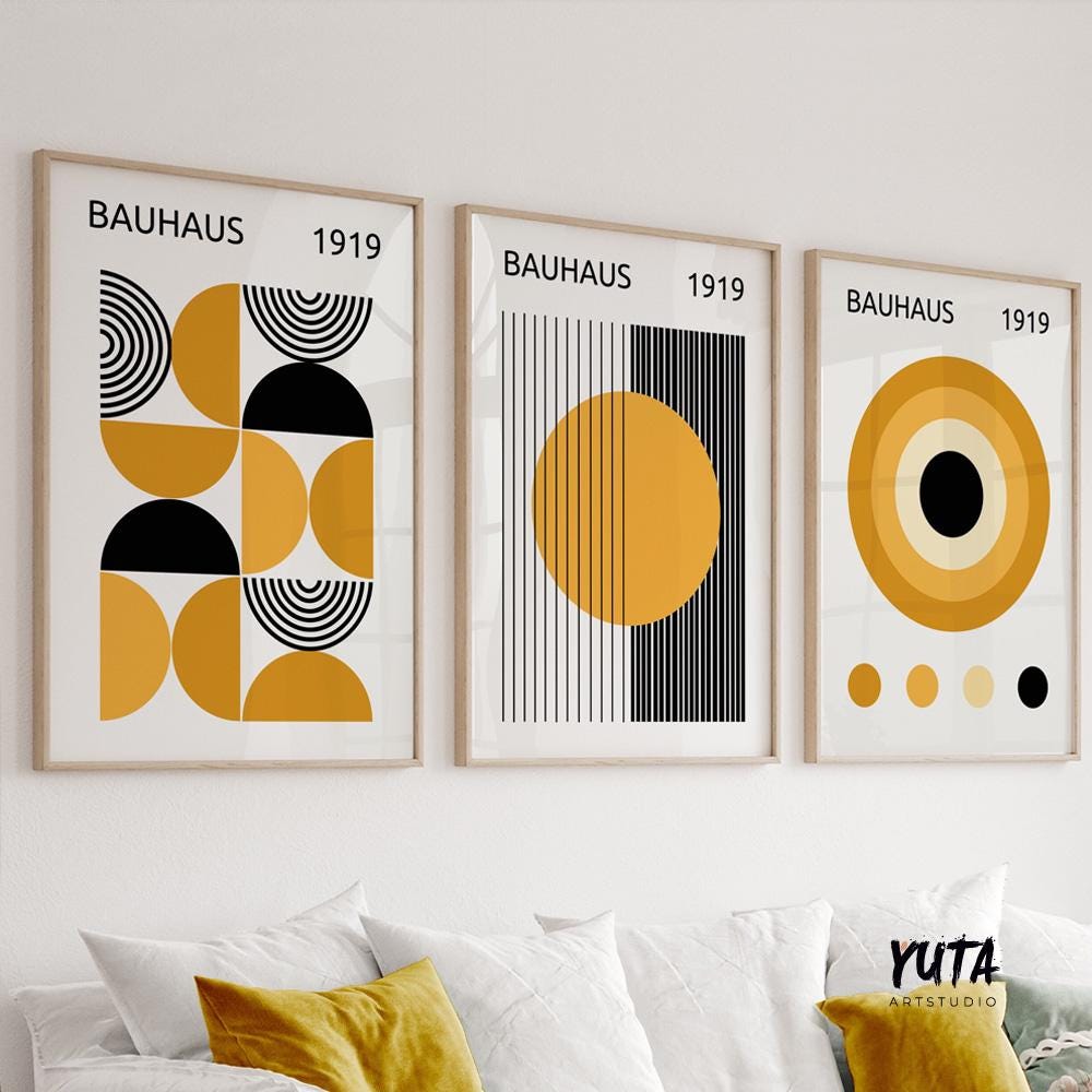 Three framed Bauhaus prints in mustard yellow and black, hung in natural daylight above a white sofa.
