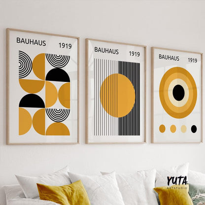 Three framed Bauhaus prints in mustard yellow and black, hung in natural daylight above a white sofa.