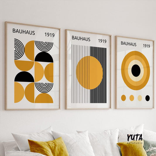 Three framed Bauhaus prints in mustard yellow and black, hung in natural daylight above a white sofa.