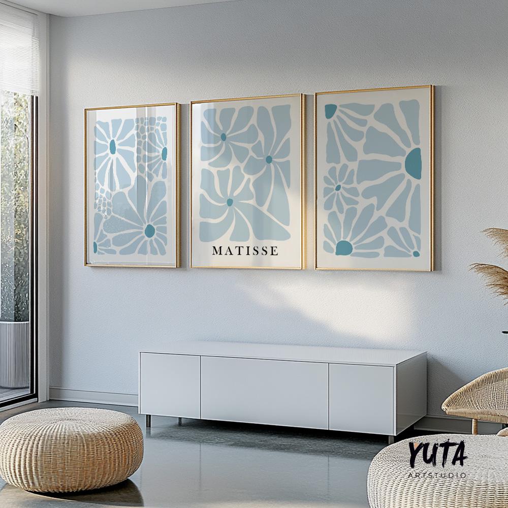 Three framed blue abstract botanical prints arranged above a low white console and rattan pouf.