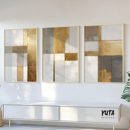 Three-piece geometric abstract art set in gold and neutral tones with visible print sizes above a console