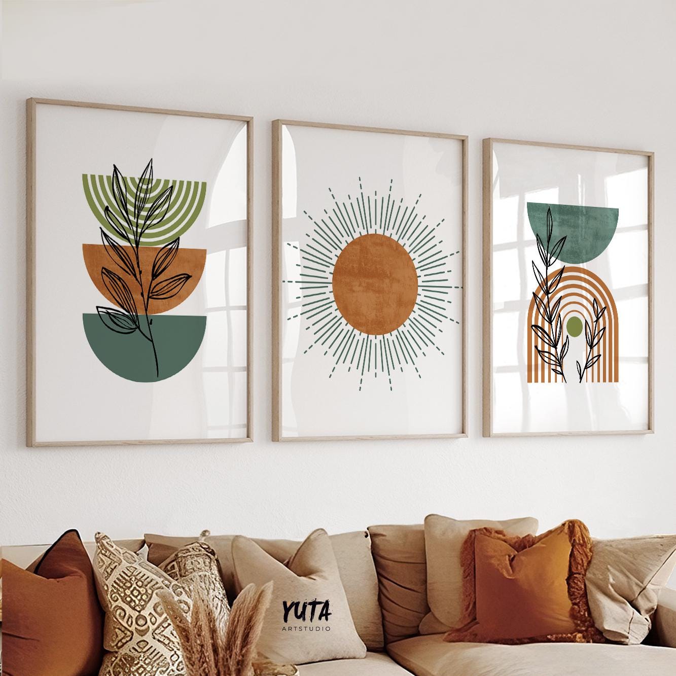 Trio of framed geometric terracotta and green boho prints styled above a sofa with patterned cushions and pampas grass.