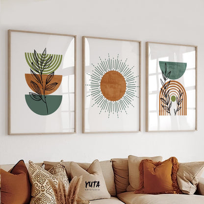 Trio of framed geometric terracotta and green boho prints styled above a sofa with patterned cushions and pampas grass.