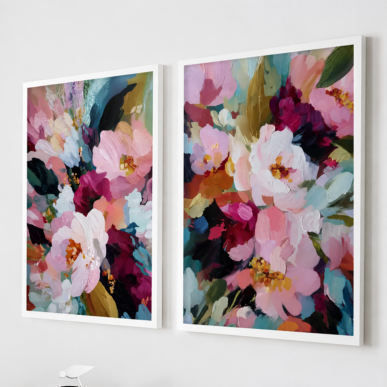 Set of two abstract floral wall art prints with pink, white, and burgundy flowers displayed in white frames on a modern living room wall.