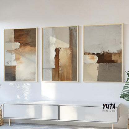 Three minimalist abstract prints in earth tones framed above a white sofa unit