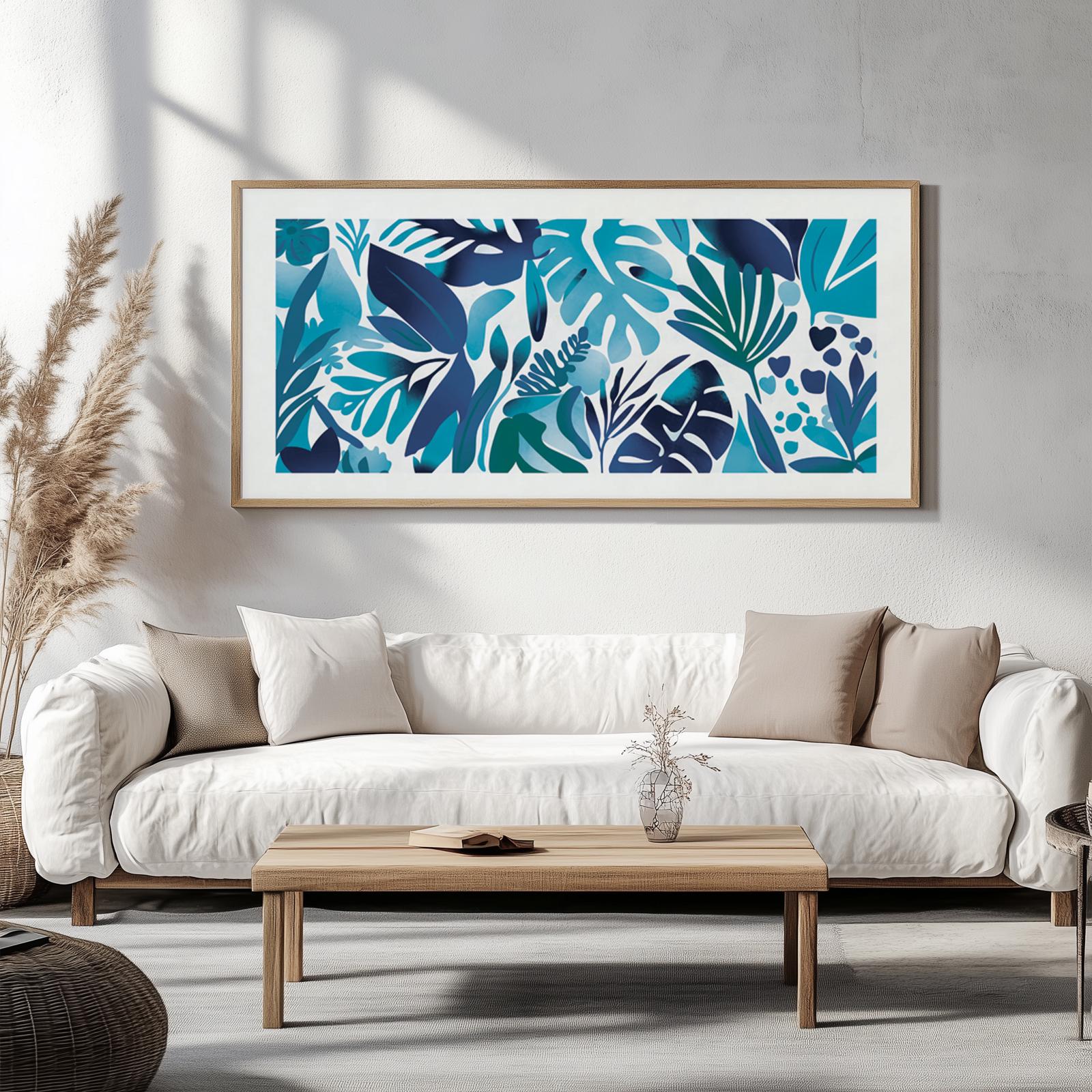 Abstract blue tropical leaves artwork in a light wood frame above a neutral sofa