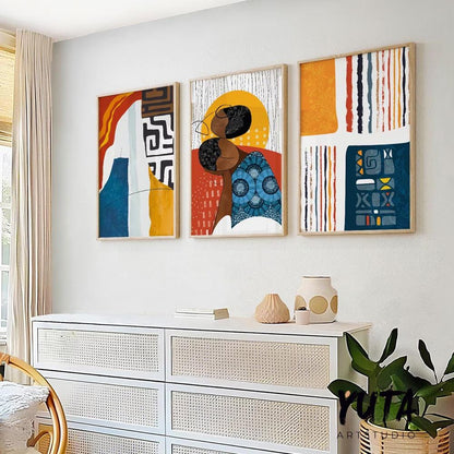 Trio of framed abstract African-inspired prints above a dresser, styled with books, ceramics, and a plant.