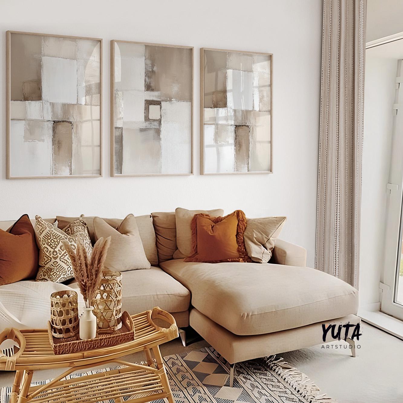 Three neutral abstract prints in light wood frames hung above a beige sectional sofa