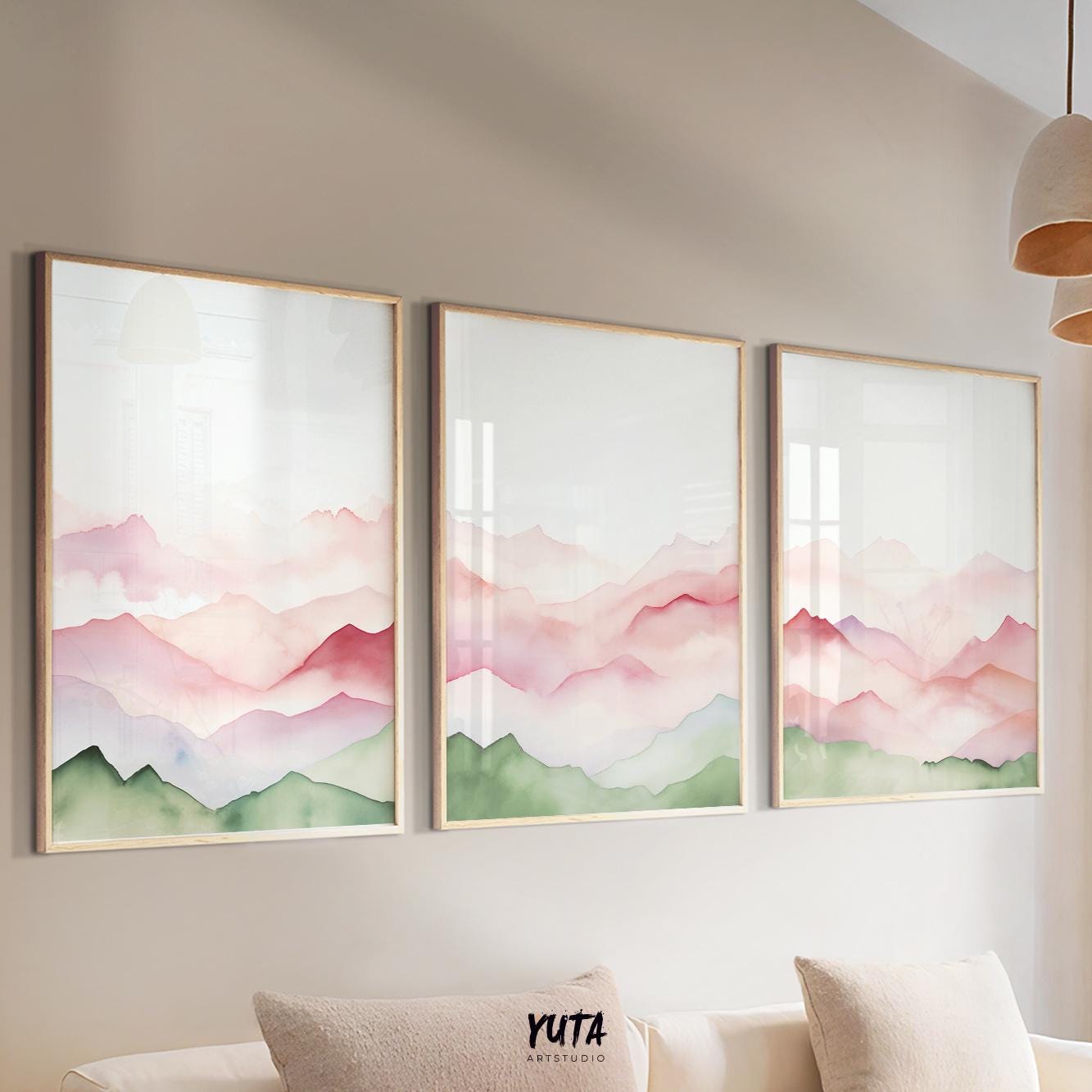 Watercolor mountain triptych in sage green and blush pink, framed and hung above a sofa