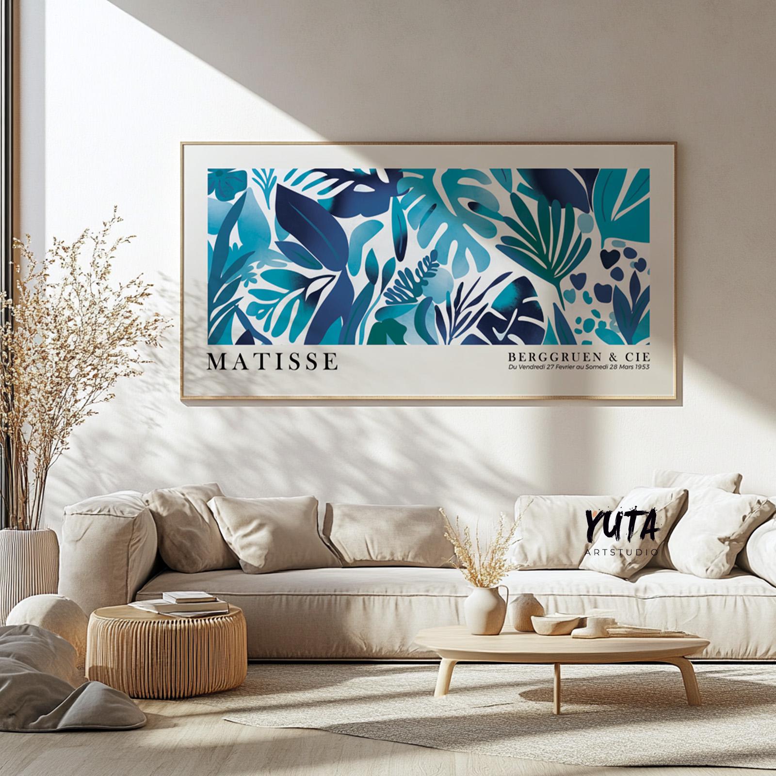Framed blue botanical Matisse-style print centered above a beige contemporary sofa