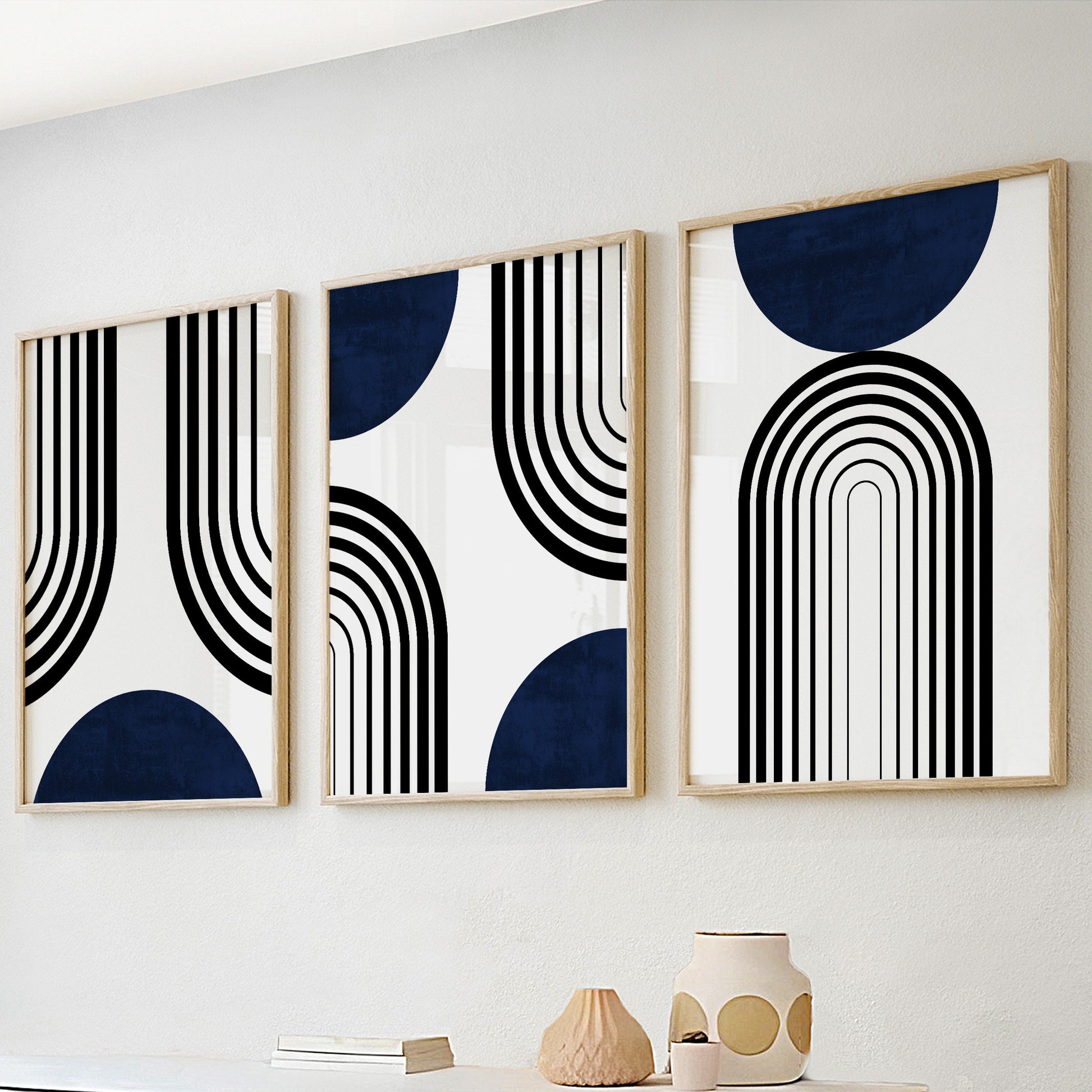 Framed navy blue and black abstract prints in three sizes displayed above a console.