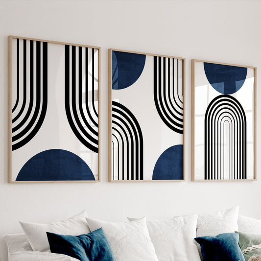Three mid-century modern abstract prints in light wood frames above a white sofa in daylight