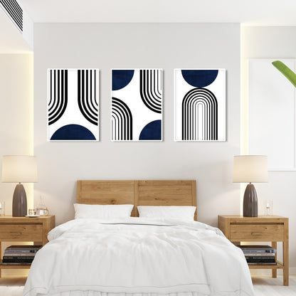 Set of three framed abstract navy blue and black prints arranged above a bed.