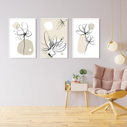 Three framed beige and black boho floral prints above a side table with books, plants, and ceramics