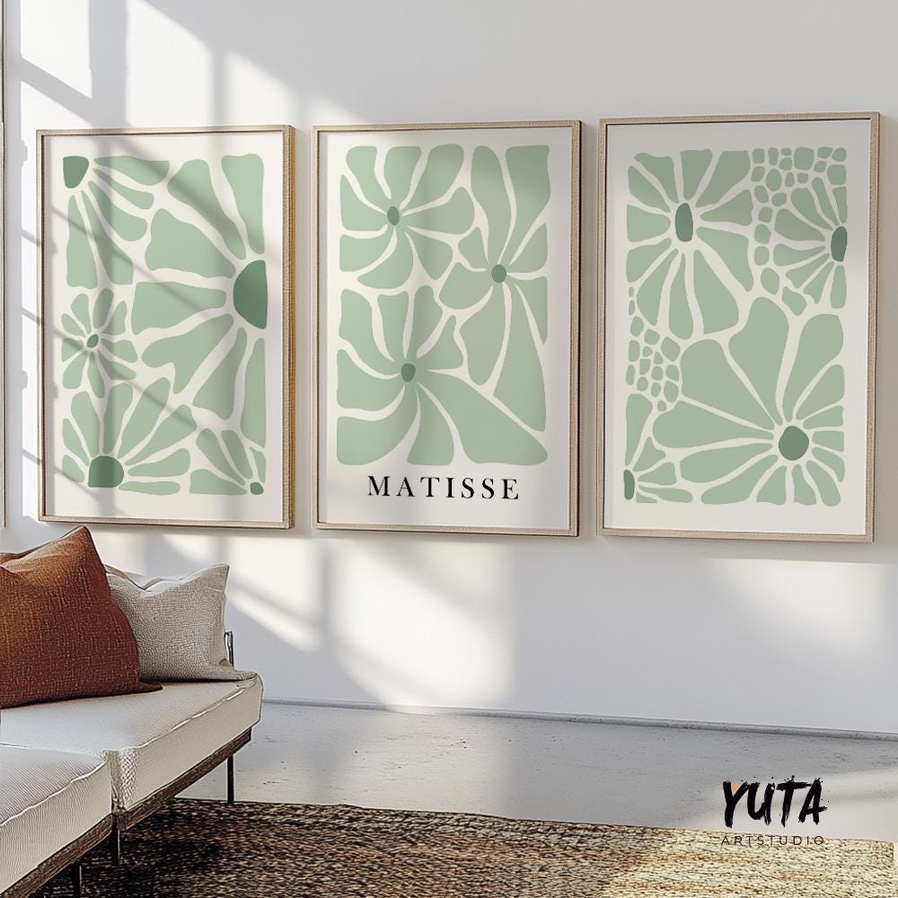 Sage green floral Matisse-inspired prints in light wood frames above a cream sofa, sunlit wall