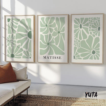 Sage green floral Matisse-inspired prints in light wood frames above a cream sofa, sunlit wall