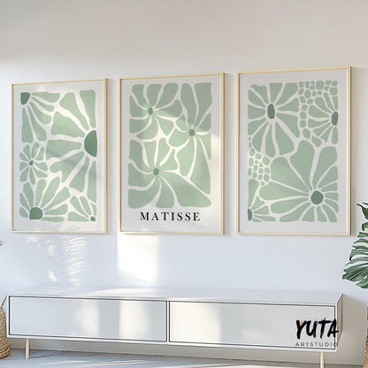 Three minimalist sage green floral prints in thin gold frames arranged above a white console