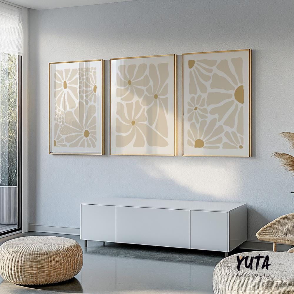 Beige abstract floral prints in gold frames above a white console with books and pampas grass.