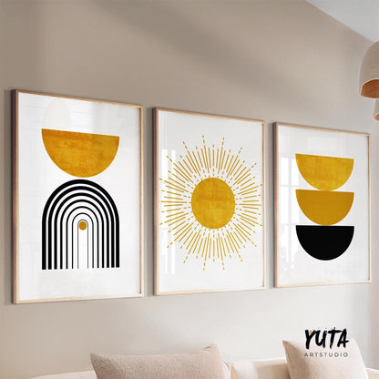 Three framed mustard yellow and black abstract prints displayed above a white sofa with books and a potted plant nearby.