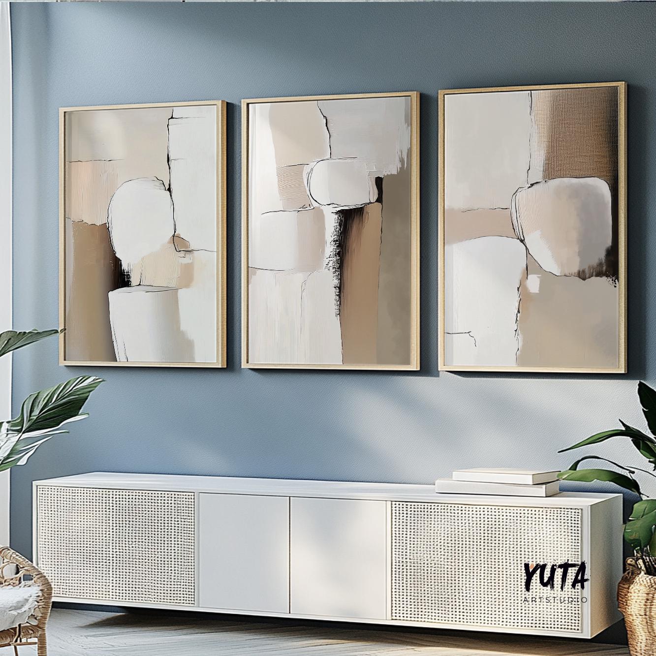 Three neutral abstract prints in light wood frames above a white console with books and plants