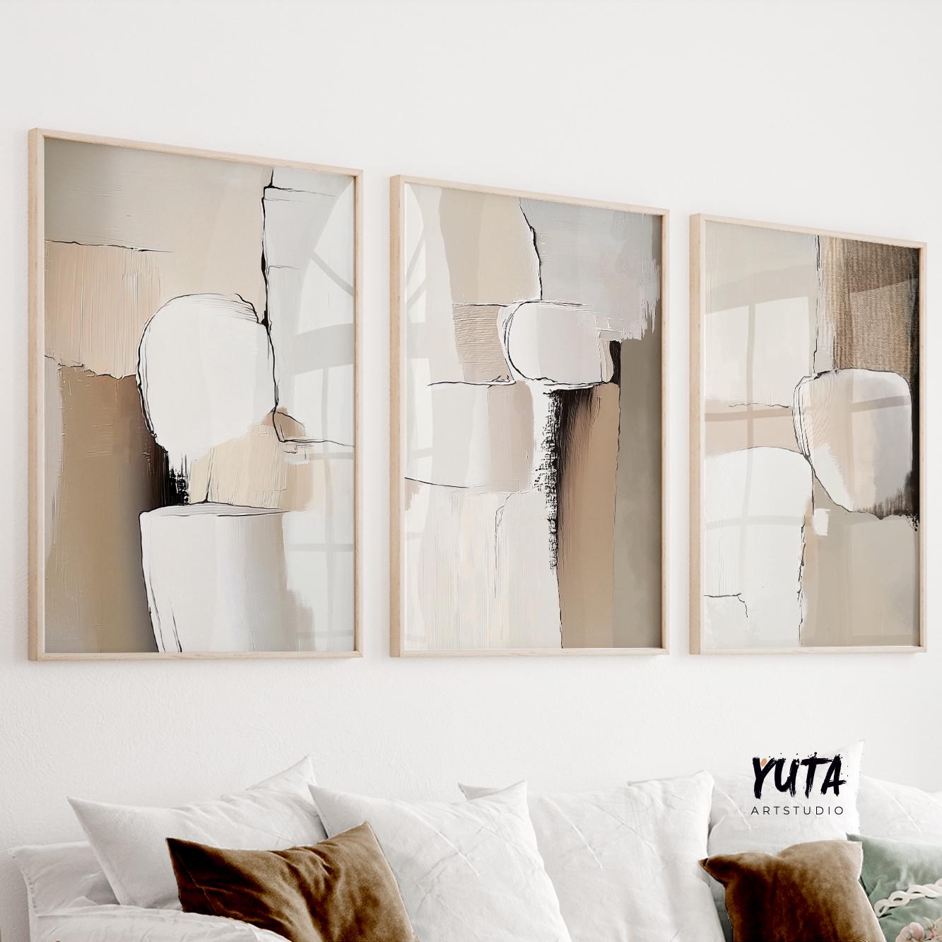 Three neutral abstract prints in light wood frames arranged above a white sofa