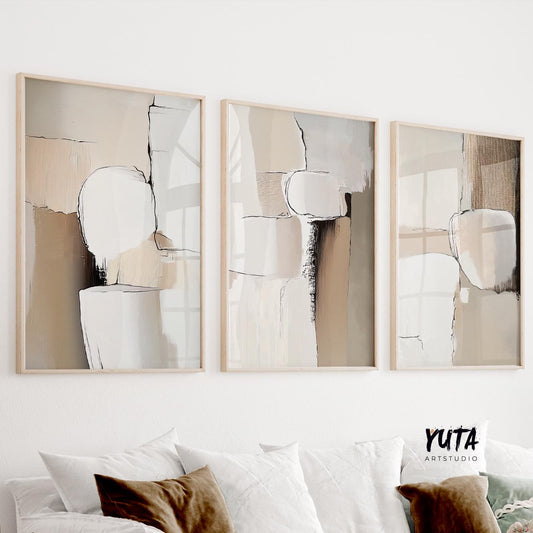 Three neutral abstract prints in light wood frames arranged above a white sofa