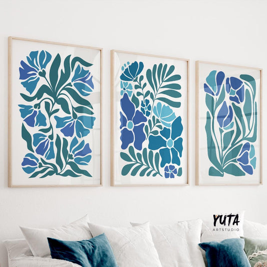 Three framed mid century floral prints with bold blue and teal botanical shapes arranged above a white sofa