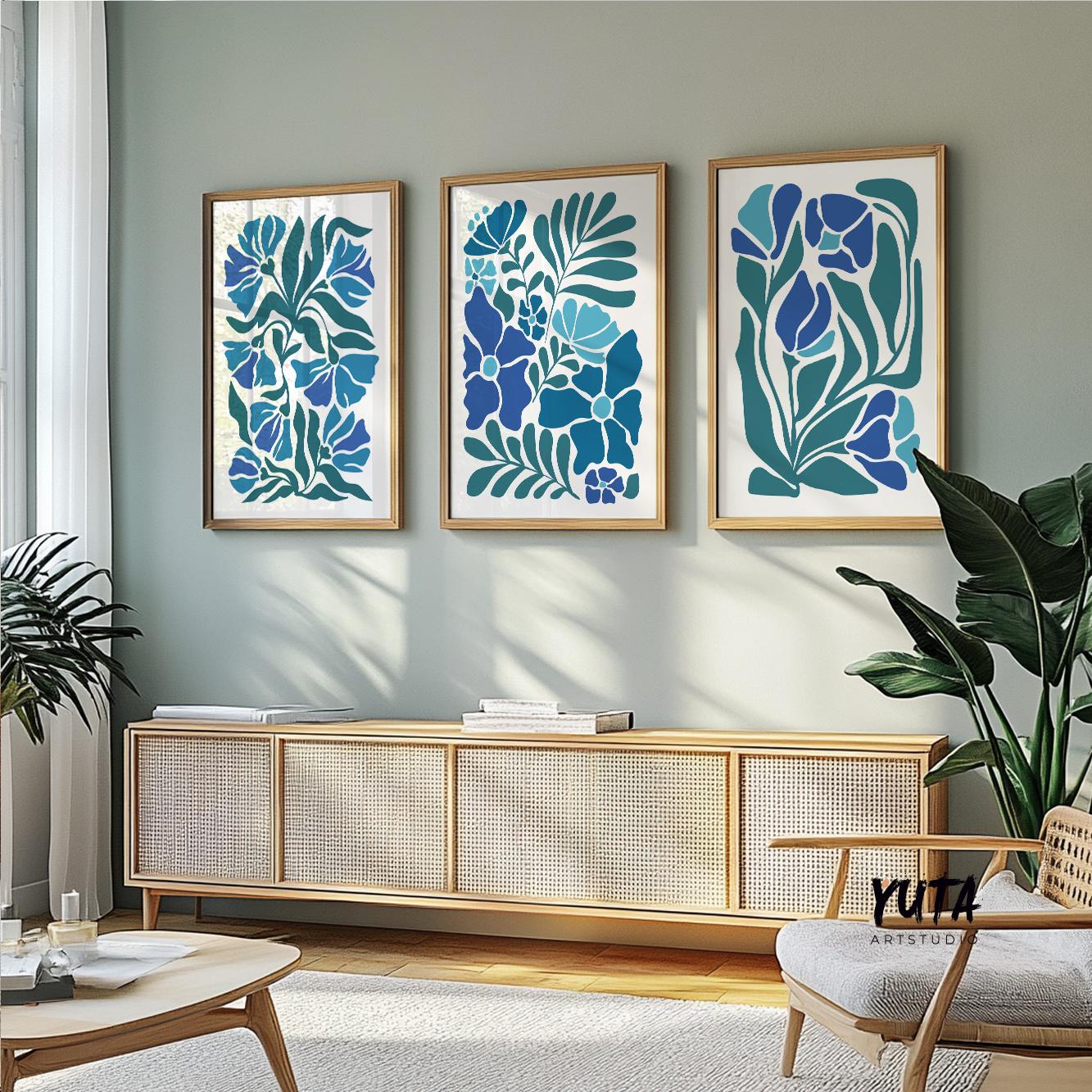 Triple panel blue botanical prints in wood frames above a sideboard with books and leafy plant