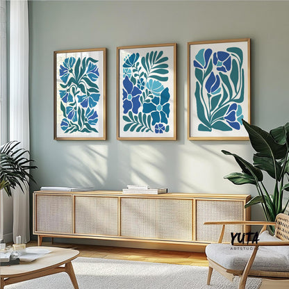Triple panel blue botanical prints in wood frames above a sideboard with books and leafy plant