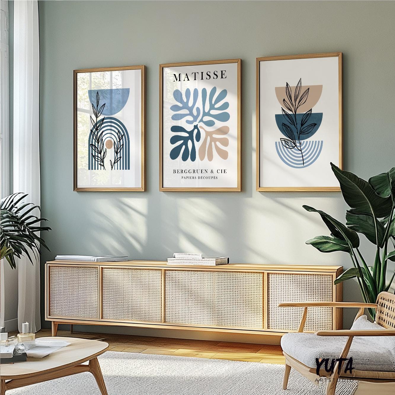 Framed abstract and botanical art trio in blue and beige above a sideboard with books and plants