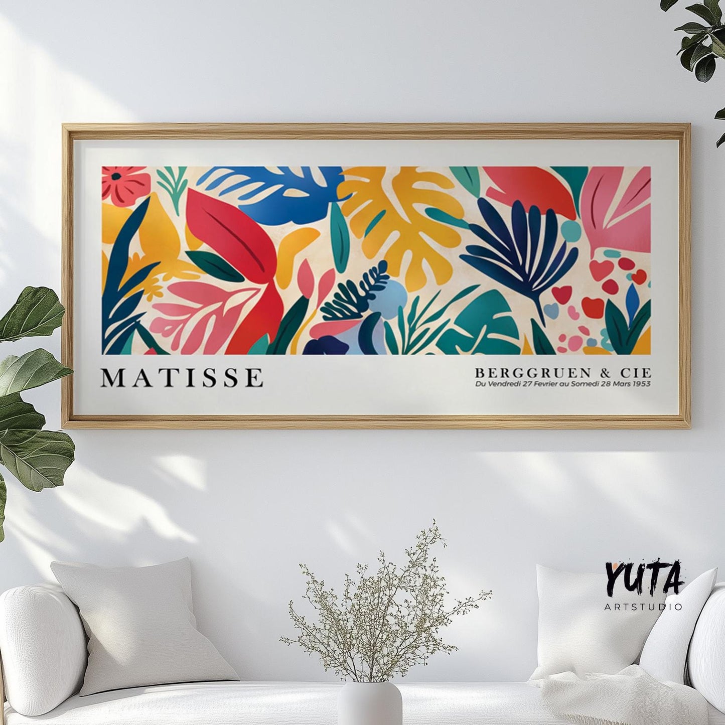 Colorful Matisse-inspired tropical foliage print in a light wood frame above a sofa with plants and a vase.