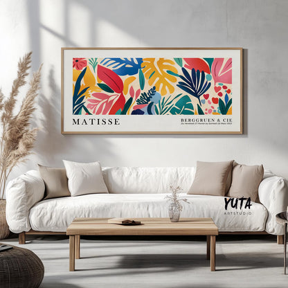 Vibrant abstract tropical leaves artwork in natural wood frame centered above a white sofa