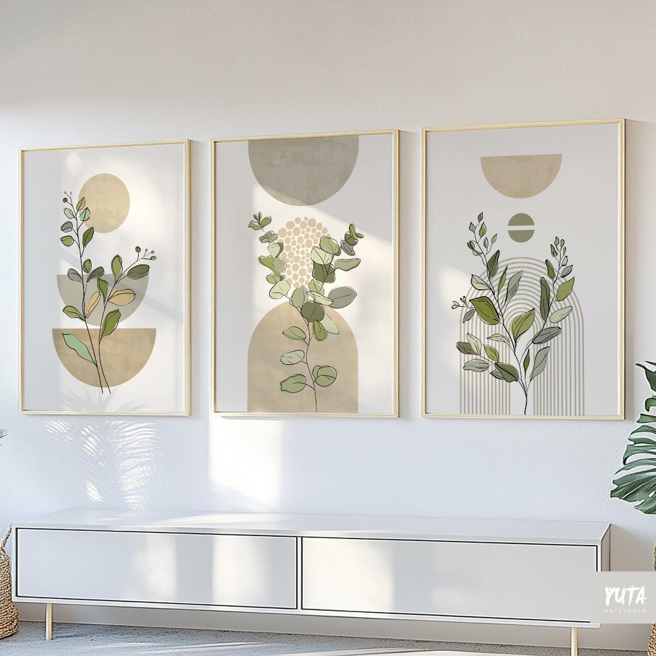Trio of sage green botanical prints with geometric shapes in light wood frames above a console