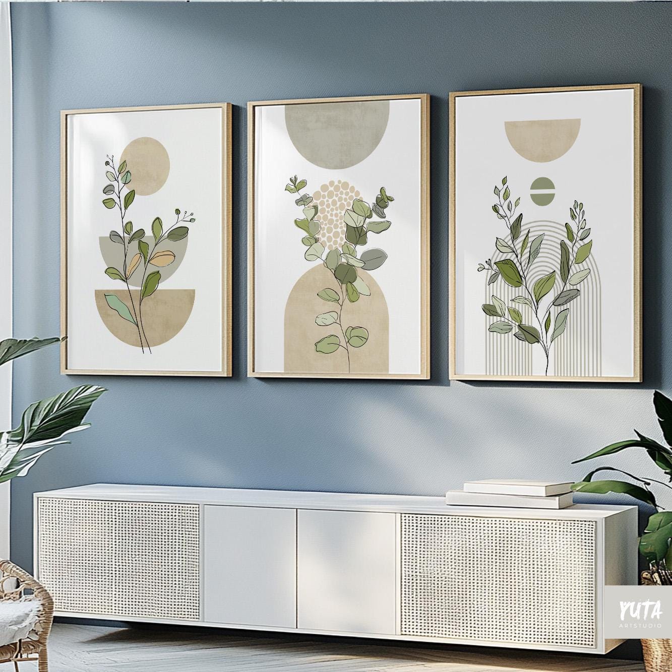 Sage green botanical prints in mid-century style wood frames arranged above a rattan sofa