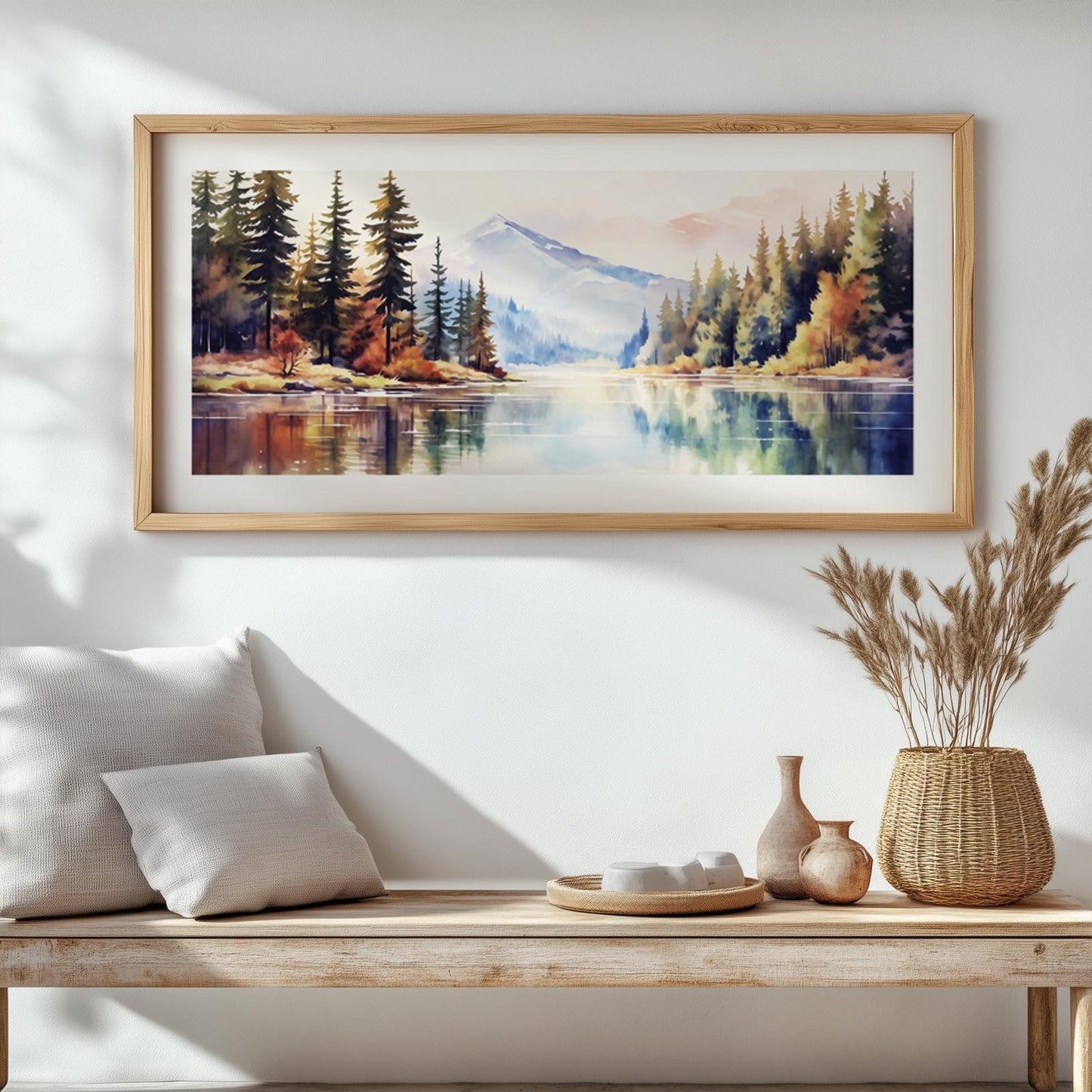 Panoramic mountain watercolor in a light wood frame above a bench with ceramics and grasses
