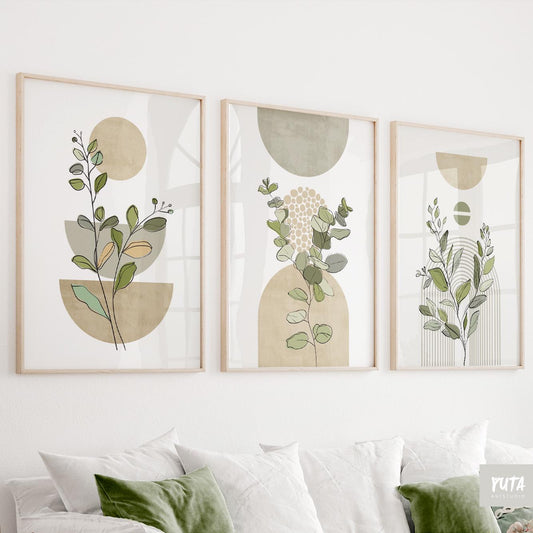 Sage green botanical prints in light oak frames displayed as a trio above a sofa.