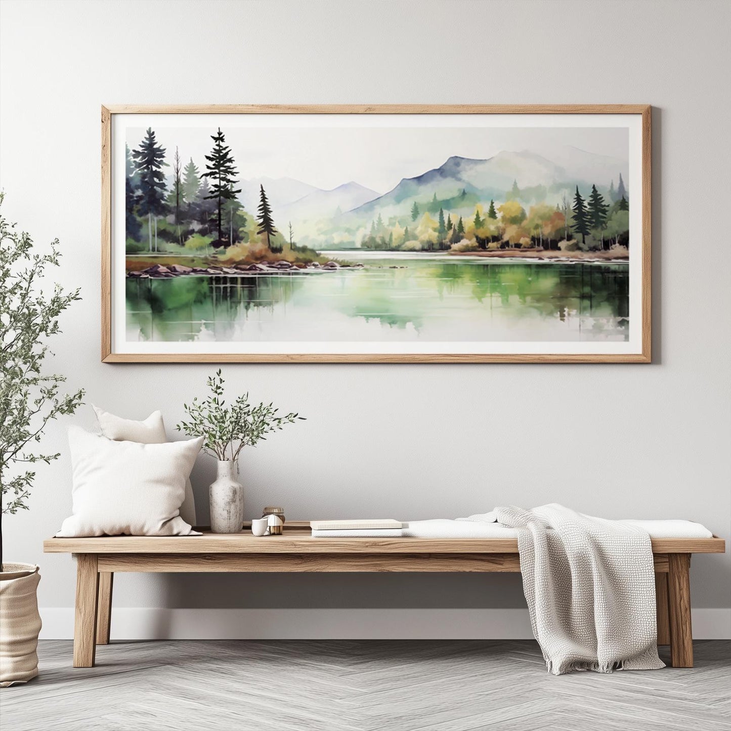 Framed watercolor forest and mountain landscape hung above a wooden bench with neutral decor