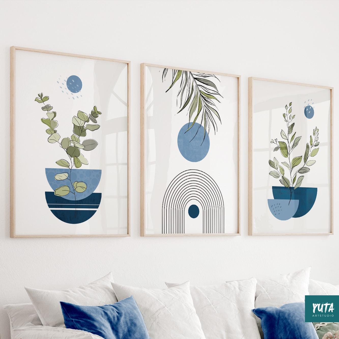 Abstract plant prints in natural wood frames styled above a white sofa with blue pillows