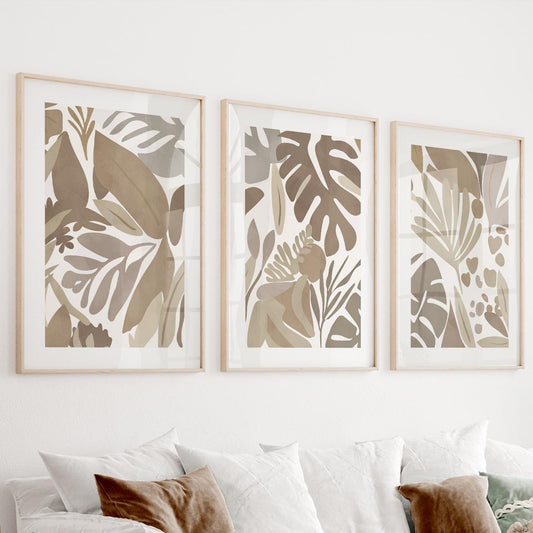 Three minimalist tropical leaf prints in natural wood frames displayed above a light sofa