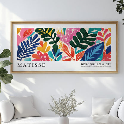 Colorful abstract leaf print in a light wood frame centered above a modern white sofa