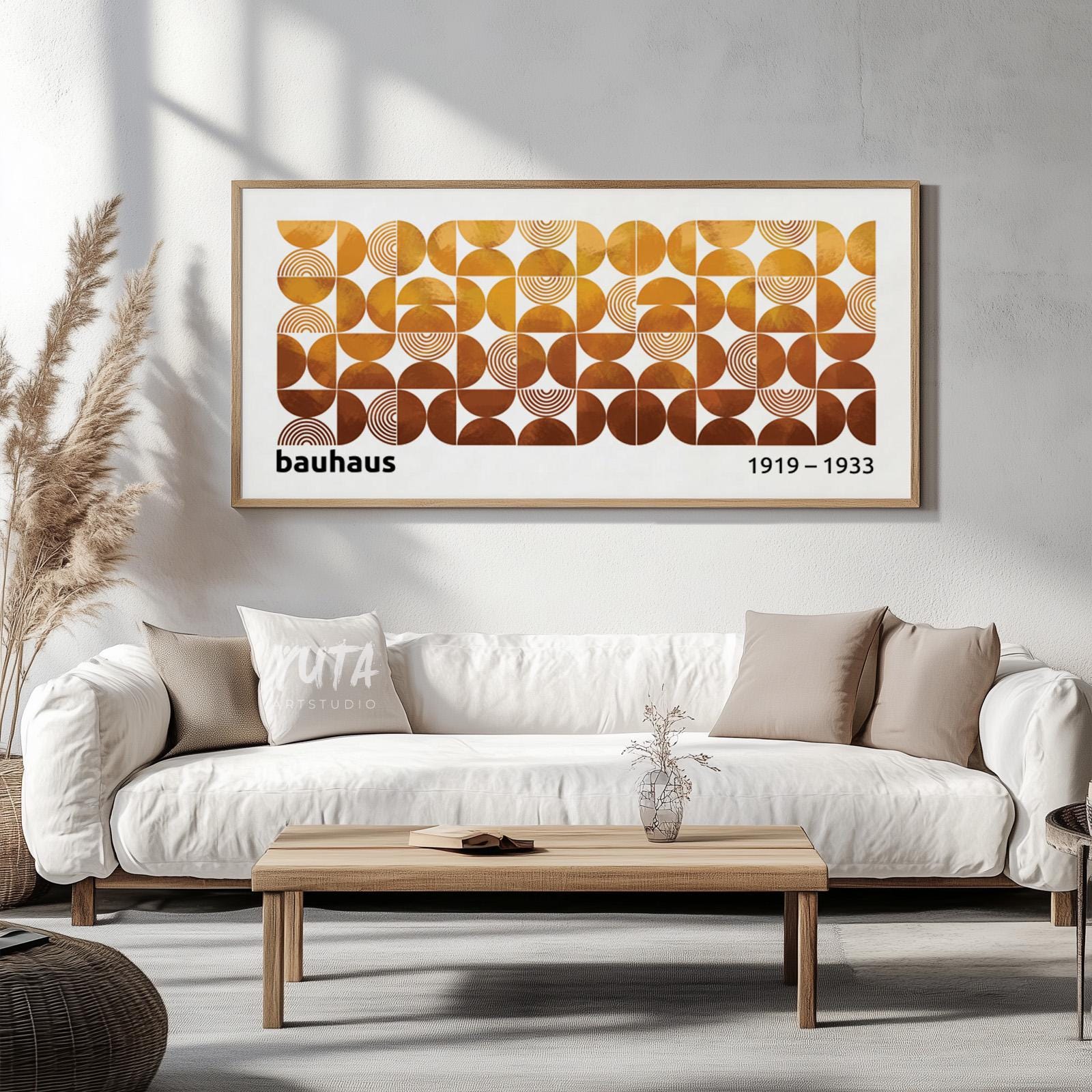 Framed geometric Bauhaus print in earth tones displayed above a white sofa in sunlit room