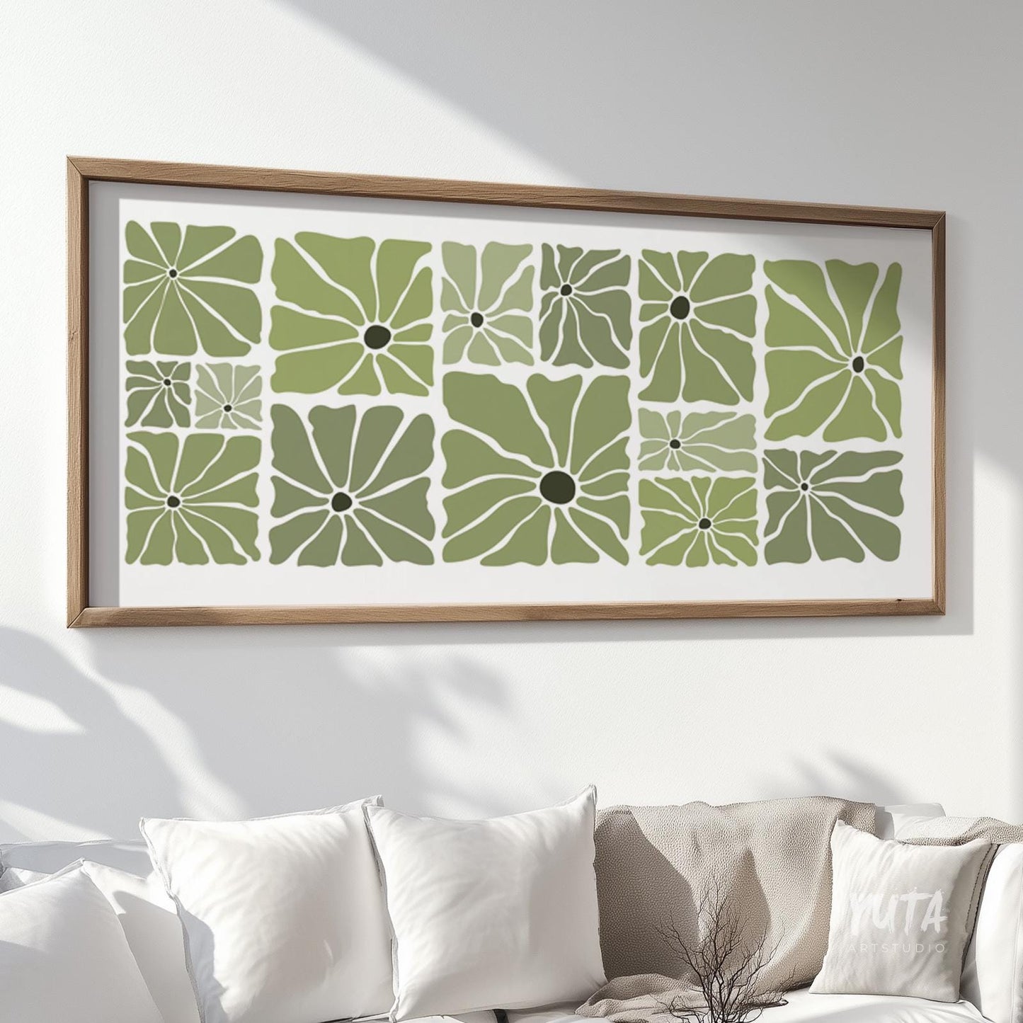 Olive green retro floral poster in a natural wood frame above a white sofa with books and ceramics.