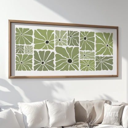 Olive green retro floral poster in a natural wood frame above a white sofa with books and ceramics.