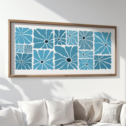 Framed blue retro floral print hung above a white sofa, illuminated by natural sunlight.