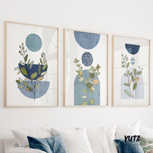Set of three framed blue botanical prints with abstract shapes arranged above a white sofa