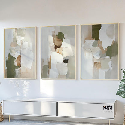 Three abstract olive green and beige prints in light wood frames above a white sideboard in sunlight