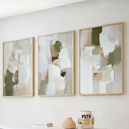 Three abstract olive green and beige prints in light wood frames above a white sofa