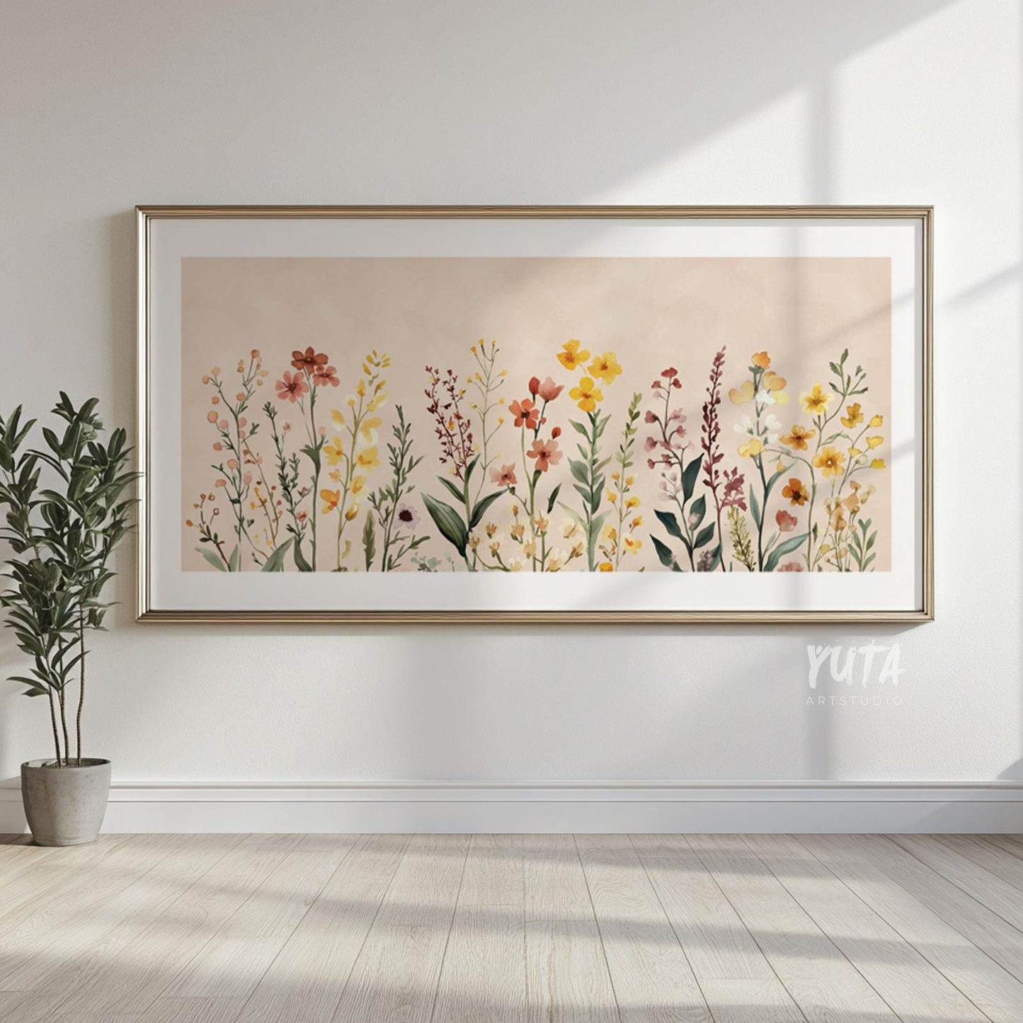 Framed neutral floral art print above light wood floors, styled with a potted plant.